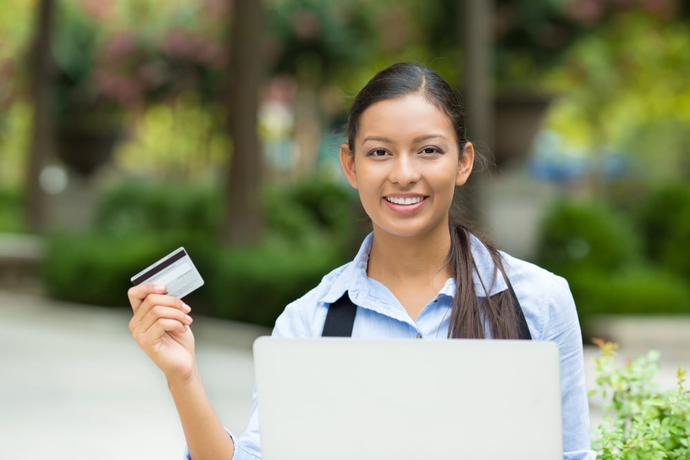 Portrait happy young business woman holding credit card and laptop making online oder, shopping concept isolated outdoors, outside background. Positive facial expressions, emotions. Smiling customer